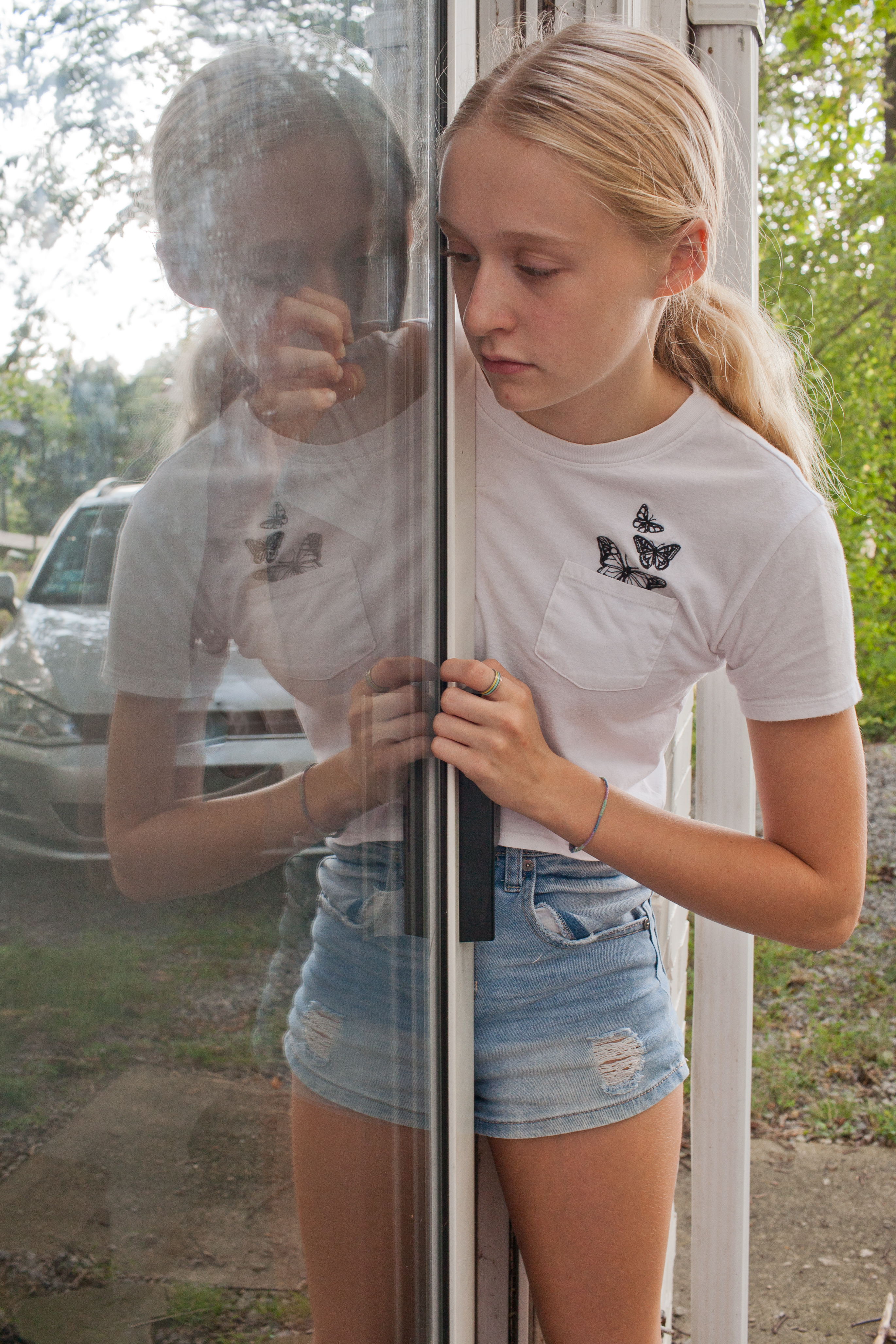 girl looking at hand through glass door